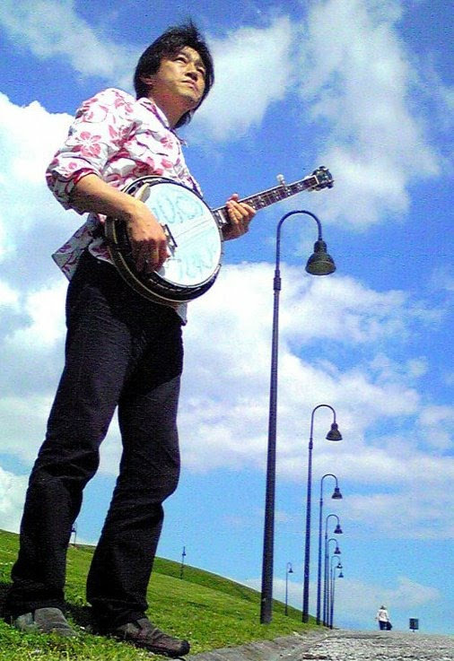 Satoshi Hara standing outdoors with his banjo